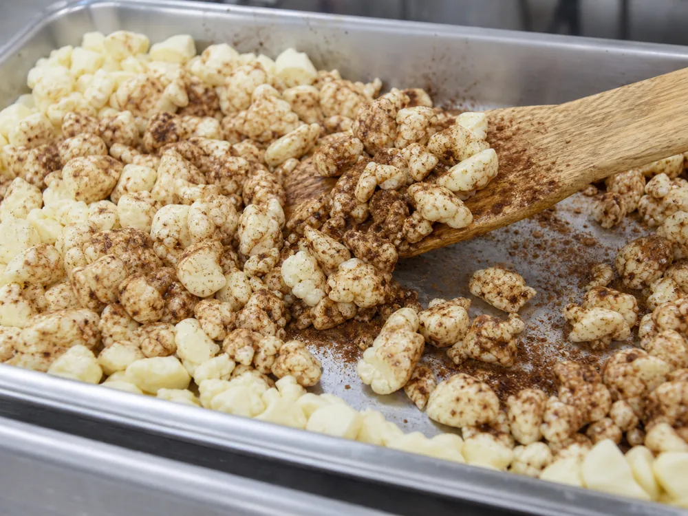 Cocoa and cinnamon mixture being folded through pale cheddar curds | KnowTheCheese