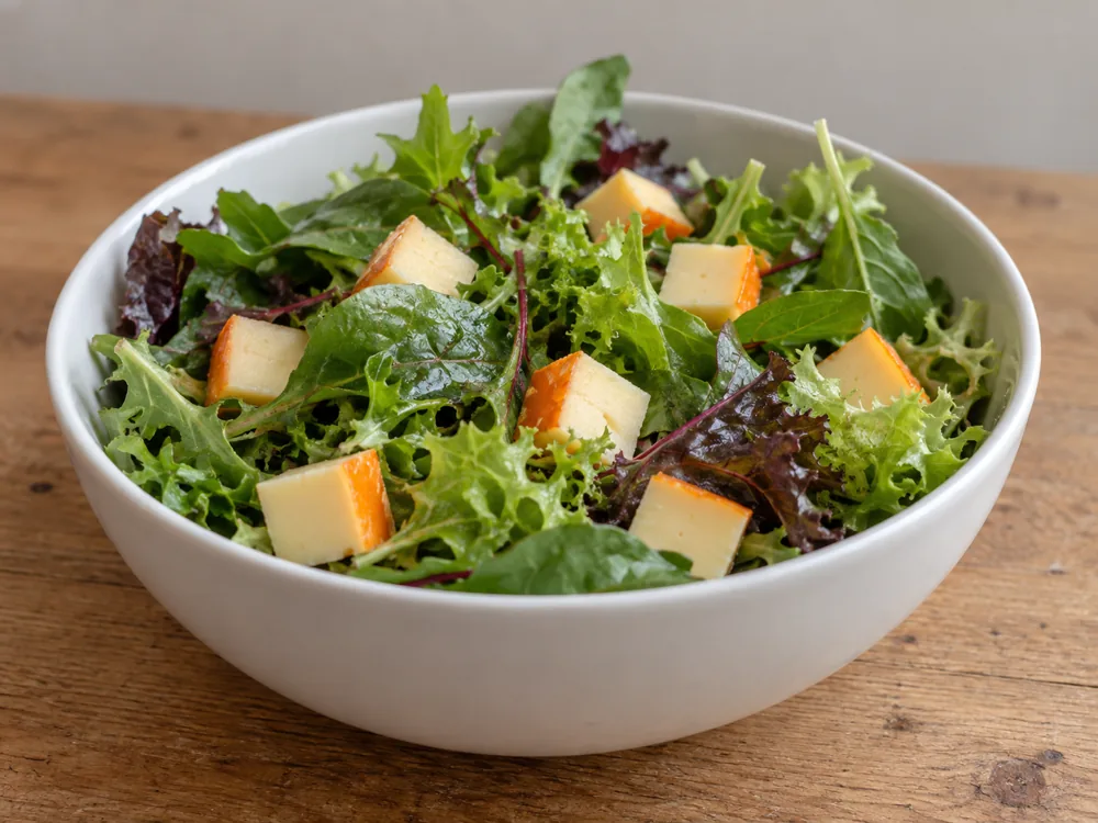 White bowl of mixed salad leaves with cubes of pale cheese showing orange rind edges - Chaumes | KnowTheCheese