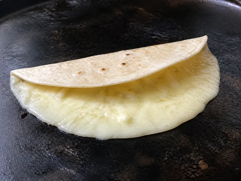 Chihuahua cheese melting evenly across a folded tortilla on a comal - Chihuahua Cheese | KnowTheCheese