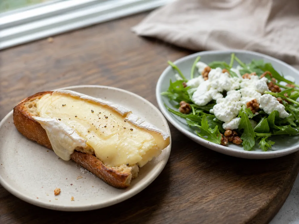 Warm melted Brie toast beside cool goat cheese crumbles over salad greens - Brie vs goat cheese | KnowTheCheese