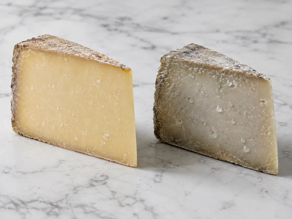 Two cut cheese wedges side by side, one matte and evenly pale and one grey with a damp surface - Comte vs Gruyere | KnowTheCheese