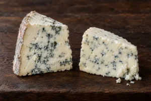 Two blue cheese wedges, one with a grey and pinkish rind and marbled veins, one crustless and evenly veined - Gorgonzola vs Roquefort | KnowTheCheese