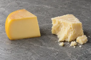 Wedge of yellow-waxed Gouda beside a crumbly piece of pale uncoloured Cheddar - Gouda vs Cheddar | KnowTheCheese