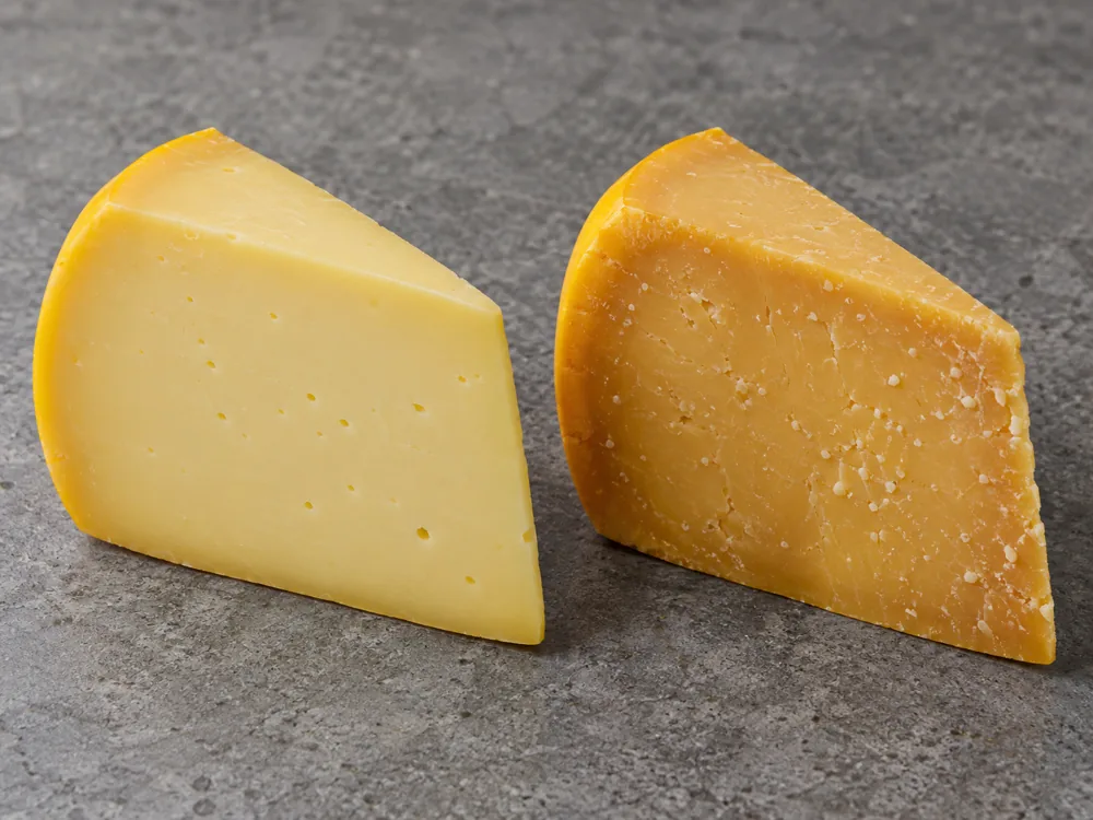 Young Gouda wedge with pale yellow paste beside an older wedge with deeper golden paste and tiny crystals - Gouda vs Cheddar | KnowTheCheese