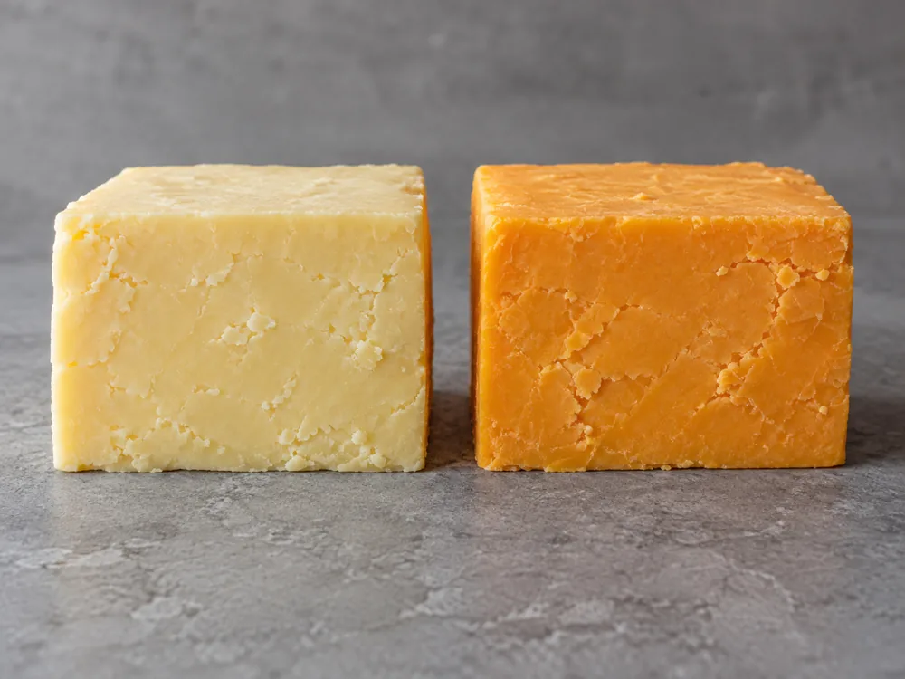 Block of off-white Cheddar beside a block of orange Cheddar, both with a firm crumbly cut face - Gouda vs Cheddar | KnowTheCheese