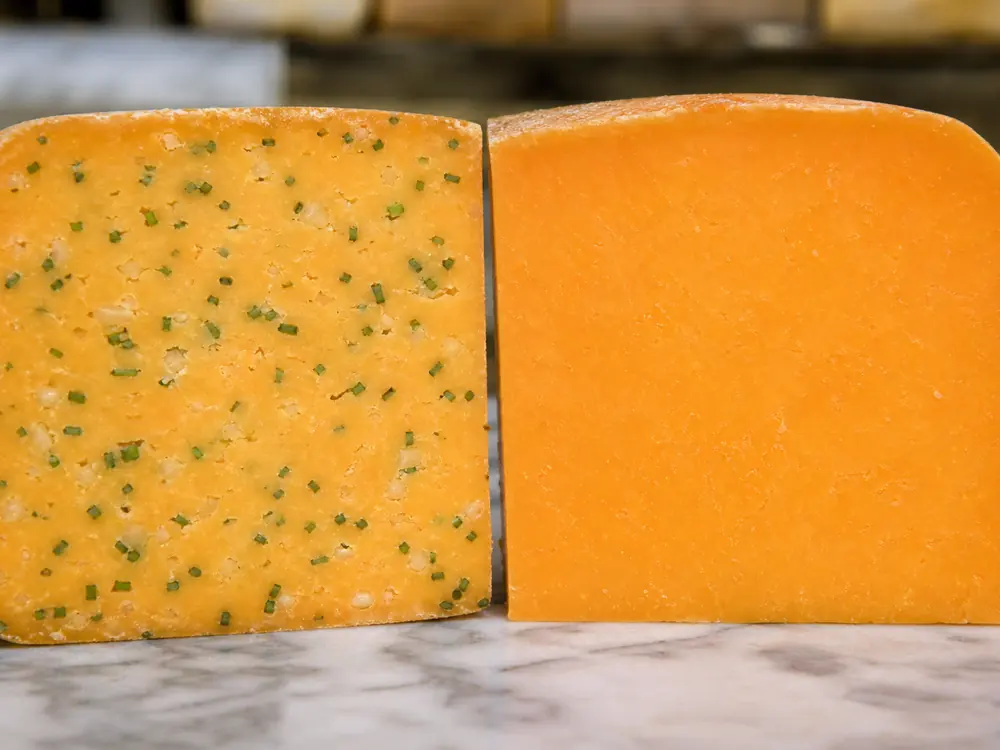 Cotswold cut face with onion pieces and green chives beside plain Double Gloucester
