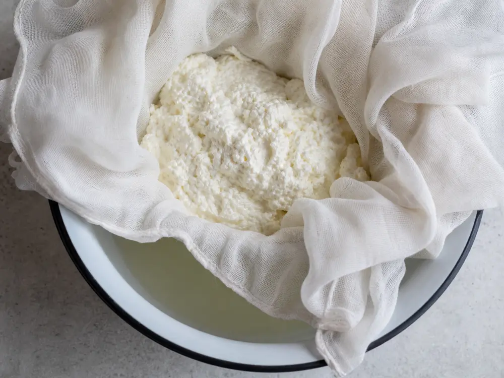 Fragile fresh lactic curd draining in muslin over a bowl - Crowdie cheese | KnowTheCheese