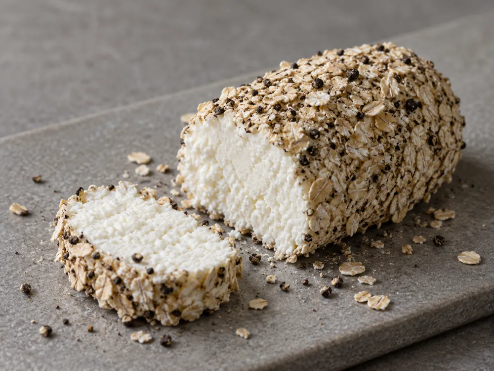 Crowdie log coated in oats and cracked black pepper with a slice cut to show the white curd - Crowdie cheese | KnowTheCheese