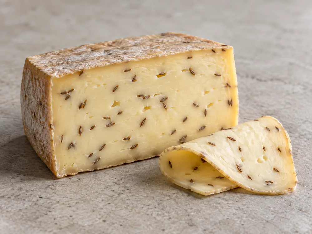 Cut block of caraway-flavoured Danbo-style cheese with seeds through the paste and a folded slice - Danbo | KnowTheCheese