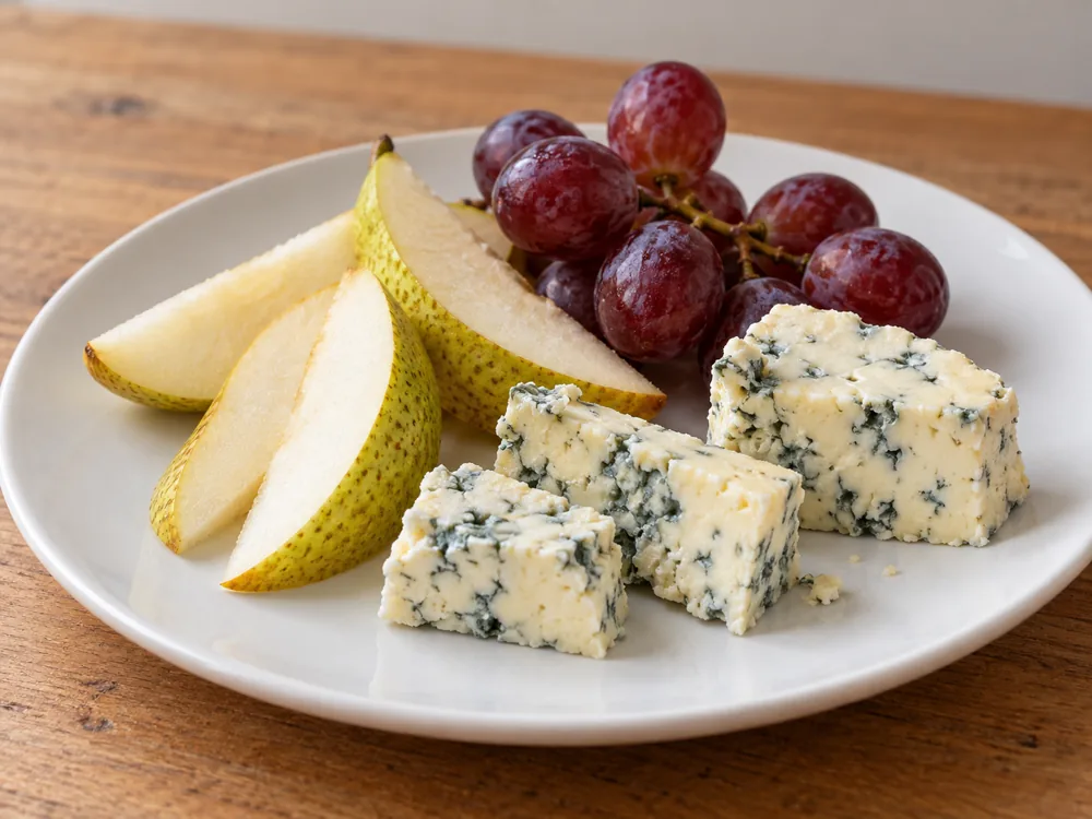 Pieces of blue-veined Danish Blue on a white plate with pear slices and red grapes - Danish Blue | KnowTheCheese