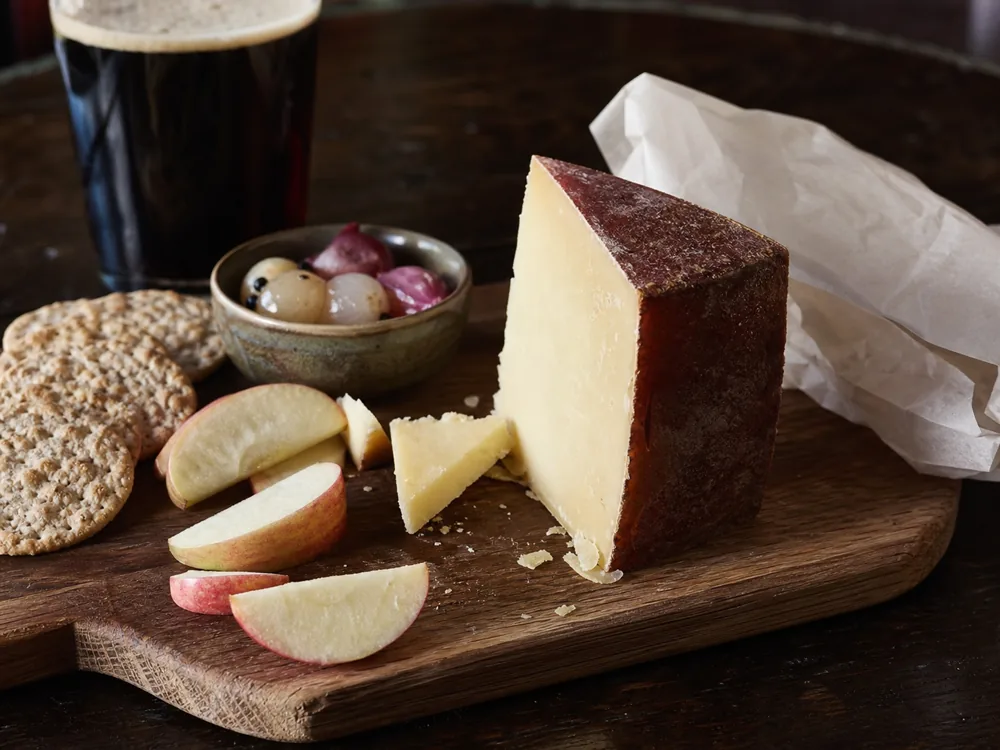 Doddington cheese on a board with apple oat crackers pickled onions and dark ale - Doddington | KnowTheCheese