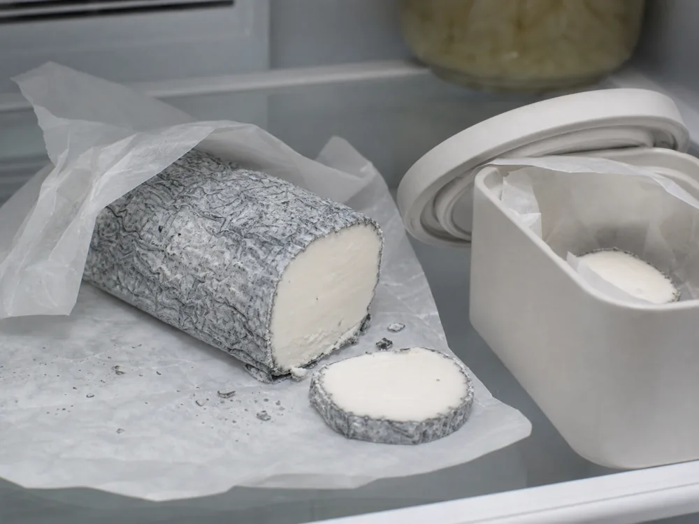 Driftwood ash coated goat cheese wrapped in wax paper with storage container - Driftwood | KnowTheCheese