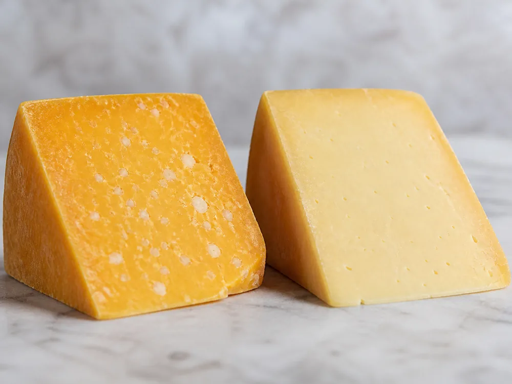Dubliner cheese wedge beside a pale Irish cheddar wedge for comparison - Dubliner cheese | KnowTheCheese