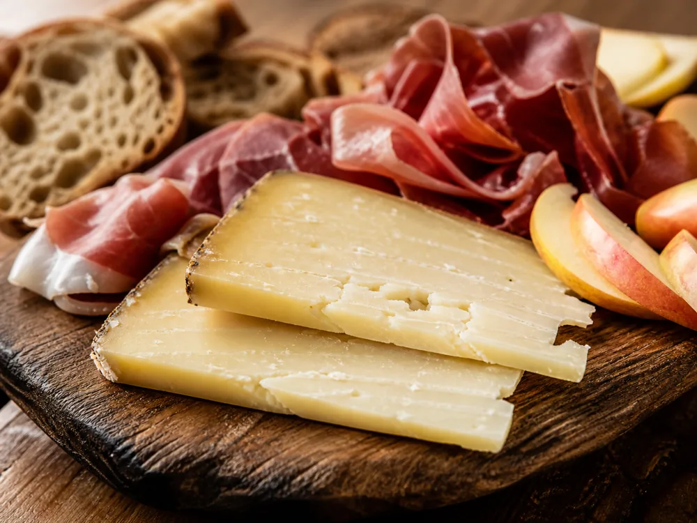 Sliced Etorki cheese on a board with ham and apple slices - Etorki cheese | KnowTheCheese
