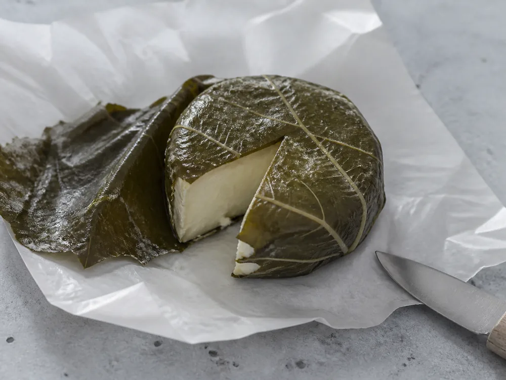 Small leaf-wrapped Figaro cheese opened on cheesemonger paper to show a moist ivory paste - Figaro | KnowTheCheese