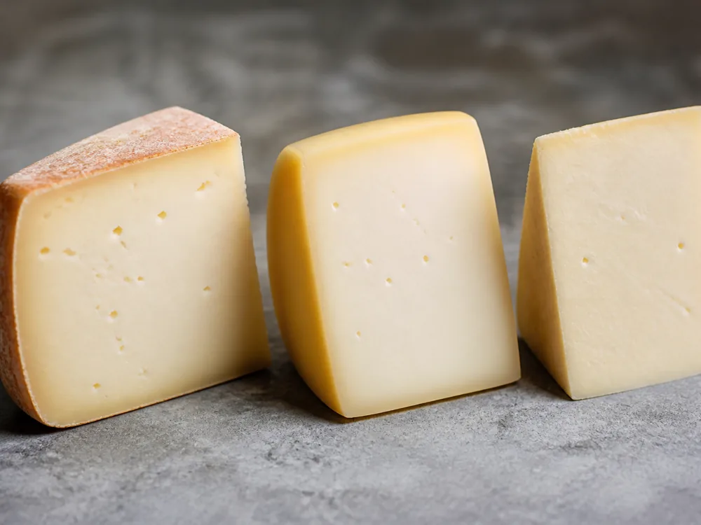 Three pale Alpine cheese wedges with a washed rind, a waxed edge and a rindless cut - Fontina | KnowTheCheese