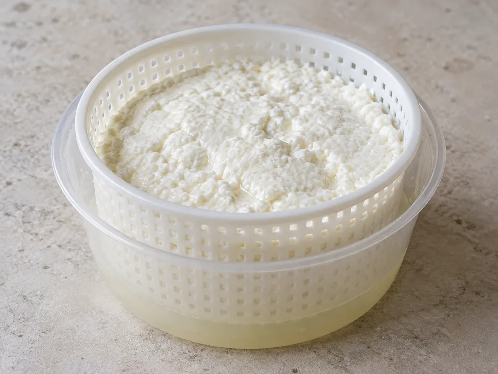 Moist white fresh curd in a perforated basket set in a pot above pale whey - Fromage Blanc | KnowTheCheese
