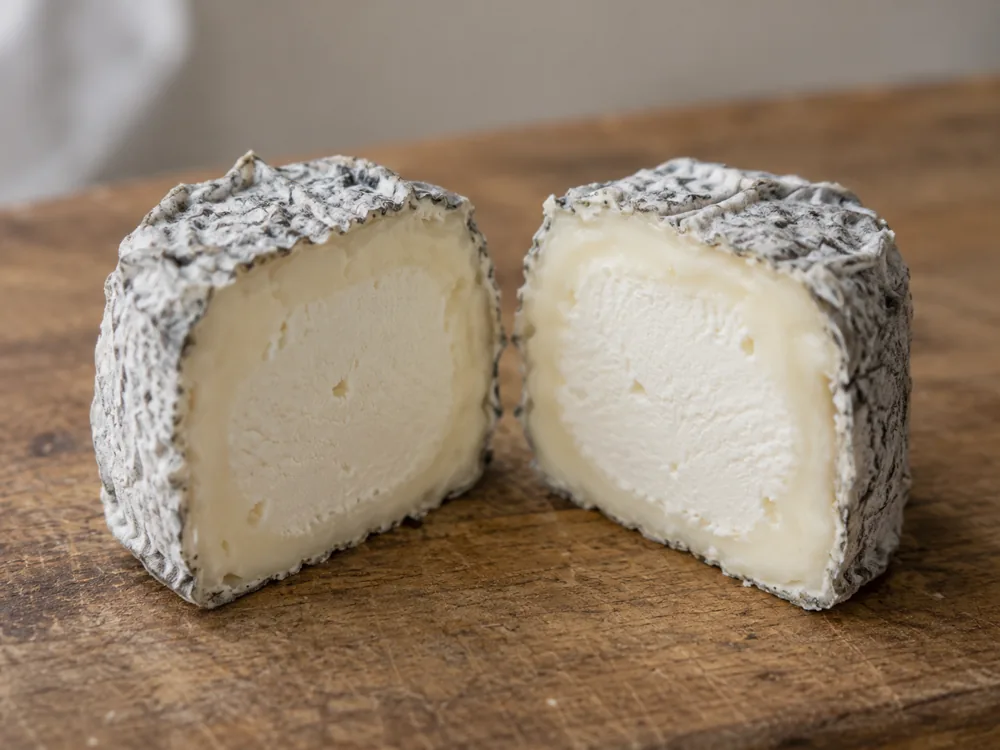Garrotxa cut in half, showing a firm pale centre and a softer, creamier band of paste under the grey rind - Garrotxa cheese | KnowTheCheese