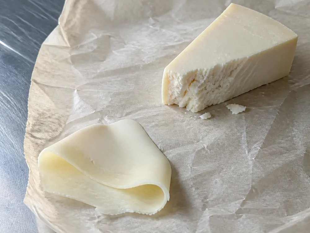 Flexible young goat Cheddar beside a crumbly aged wedge on cheesemonger paper - Goat Cheddar | KnowTheCheese