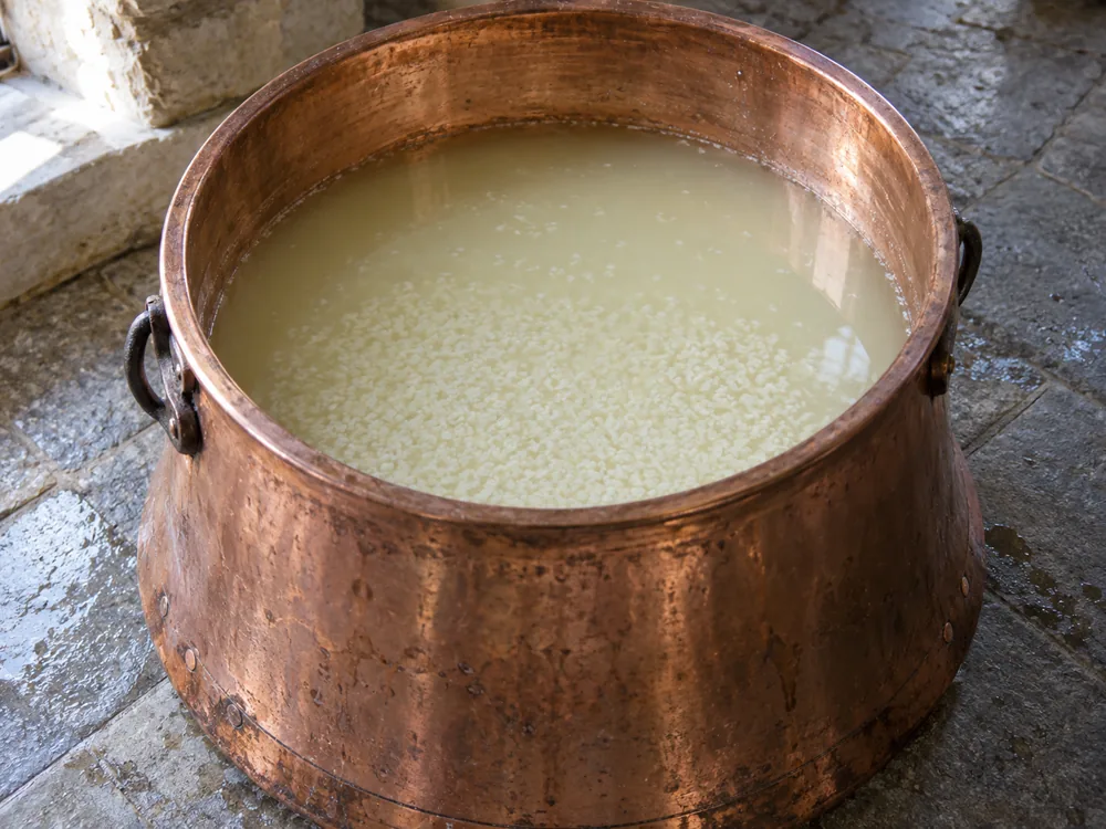 Copper cheese vat of whey holding small curd granules - Grana Padano | KnowTheCheese