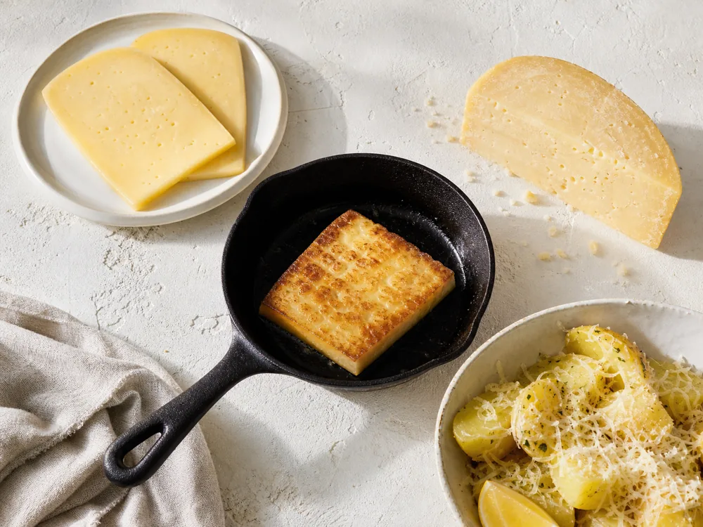 Graviera table slices, browned skillet piece, and grated cheese on potatoes - Graviera | KnowTheCheese