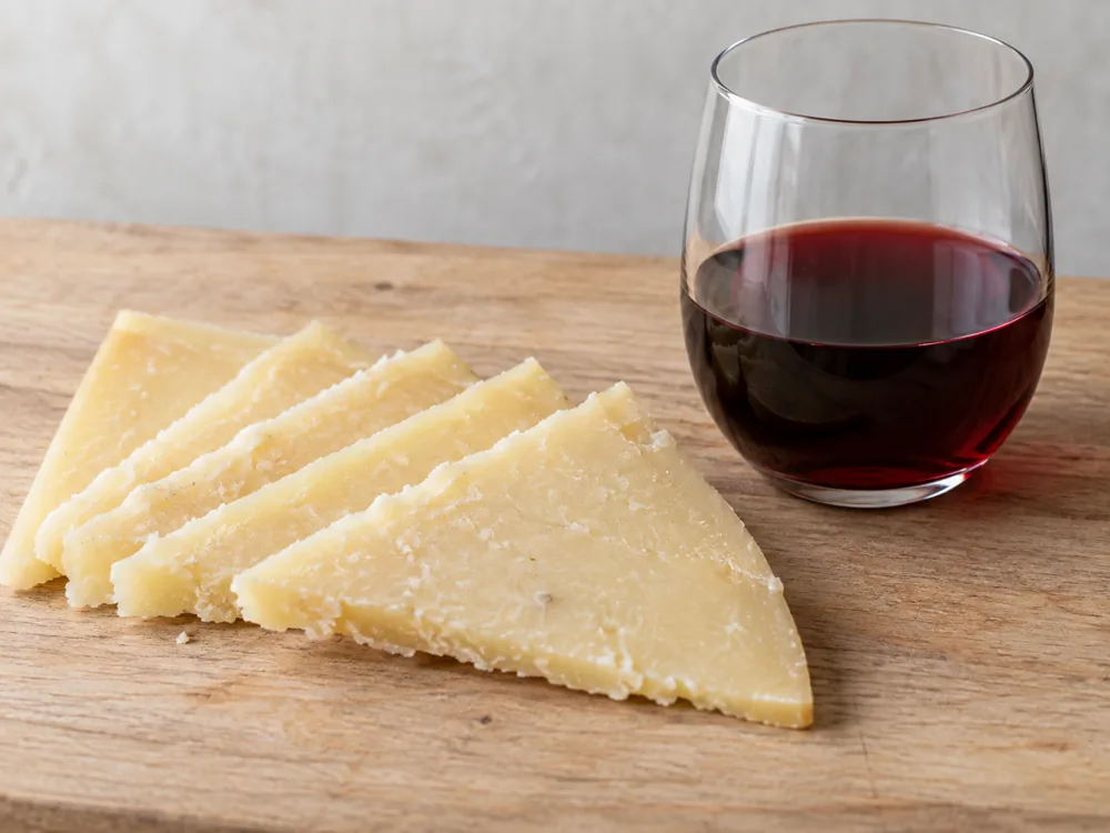 Thin slices of Graviera beside a glass of red wine - Graviera | KnowTheCheese