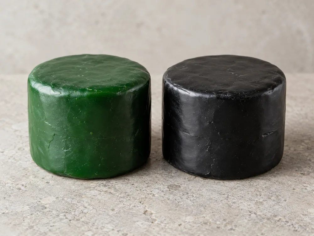 Two cheese truckles side by side, one in emerald-green wax and one in black wax - Green Thunder cheese | KnowTheCheese