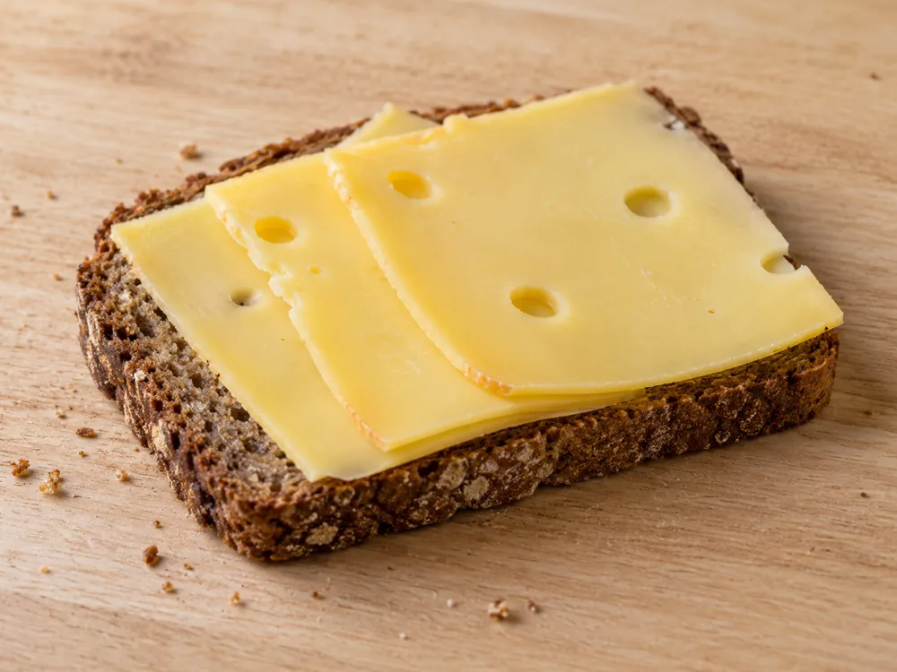 Thin slices of golden-yellow cheese on a slice of rye bread - Greve cheese | KnowTheCheese