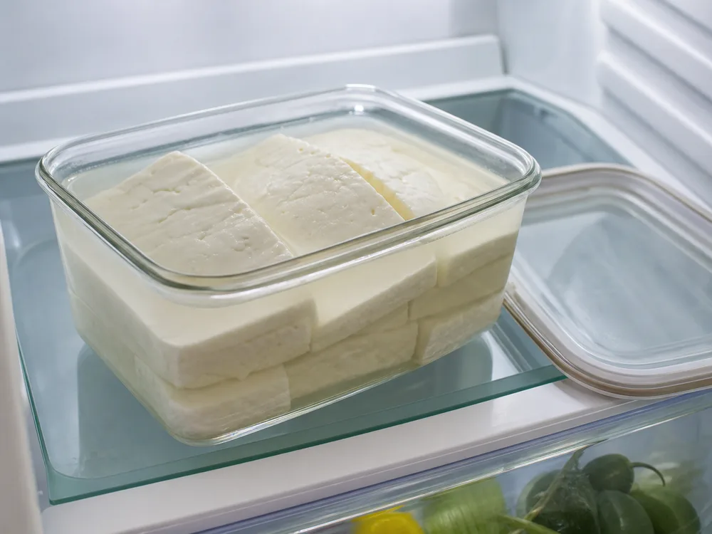 Opened glass container with Halloumi slabs fully submerged in brine in a refrigerator - Halloumi | KnowTheCheese