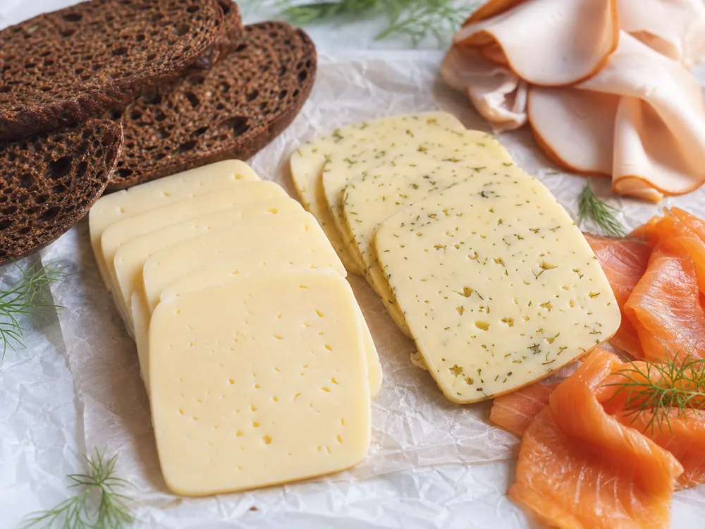 Plain Havarti and dill Havarti slices showing tiny eyes and herb flecks - Havarti cheese | KnowTheCheese