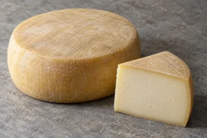Whole cylindrical cheese with a pale yellow rind beside a cut wedge of ivory paste - Idiazabal | KnowTheCheese