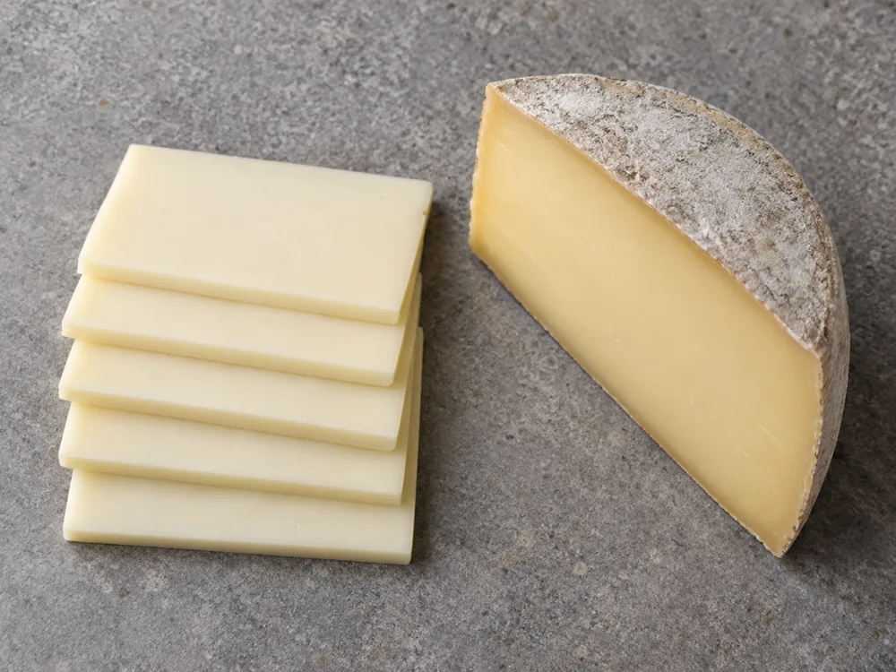 Stack of pale cream cheese slices beside an aged wedge with a grayish rind - Kashar cheese | KnowTheCheese