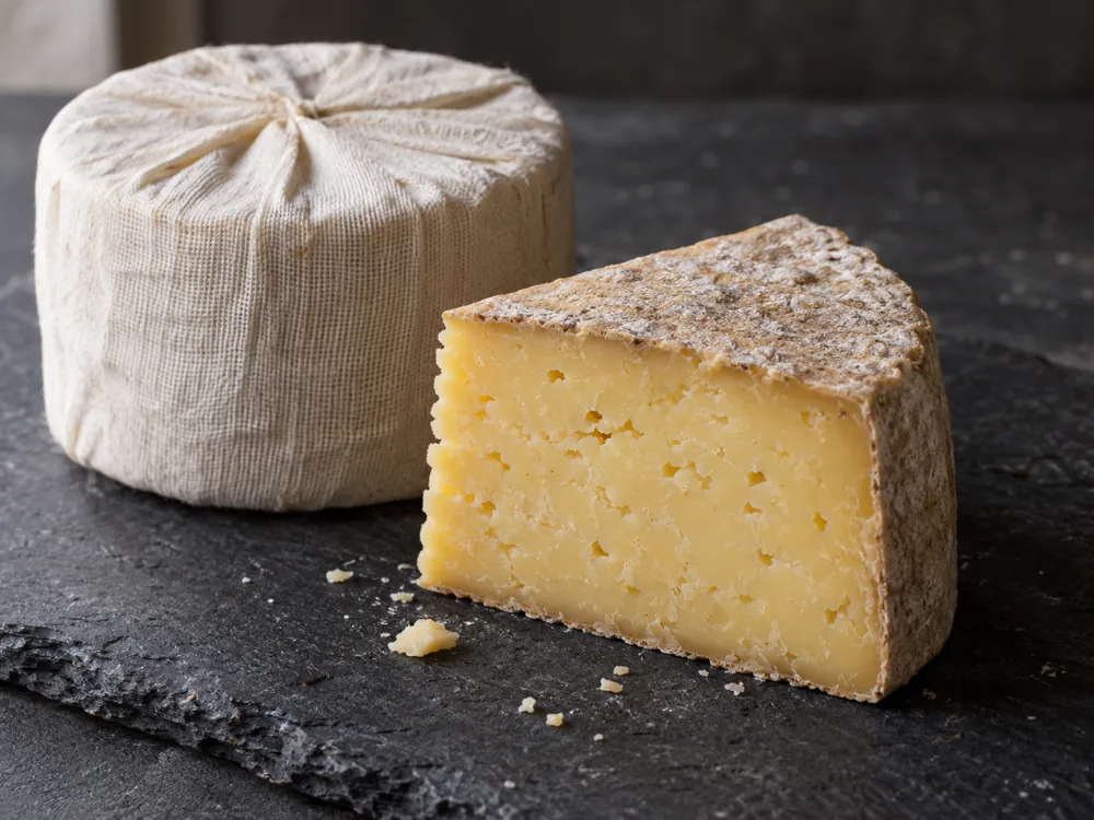 Illustration of a cloth-bound Cheddar truckle beside a cut wedge with rind and creamy yellow paste - Keen's Cheddar | KnowTheCheese