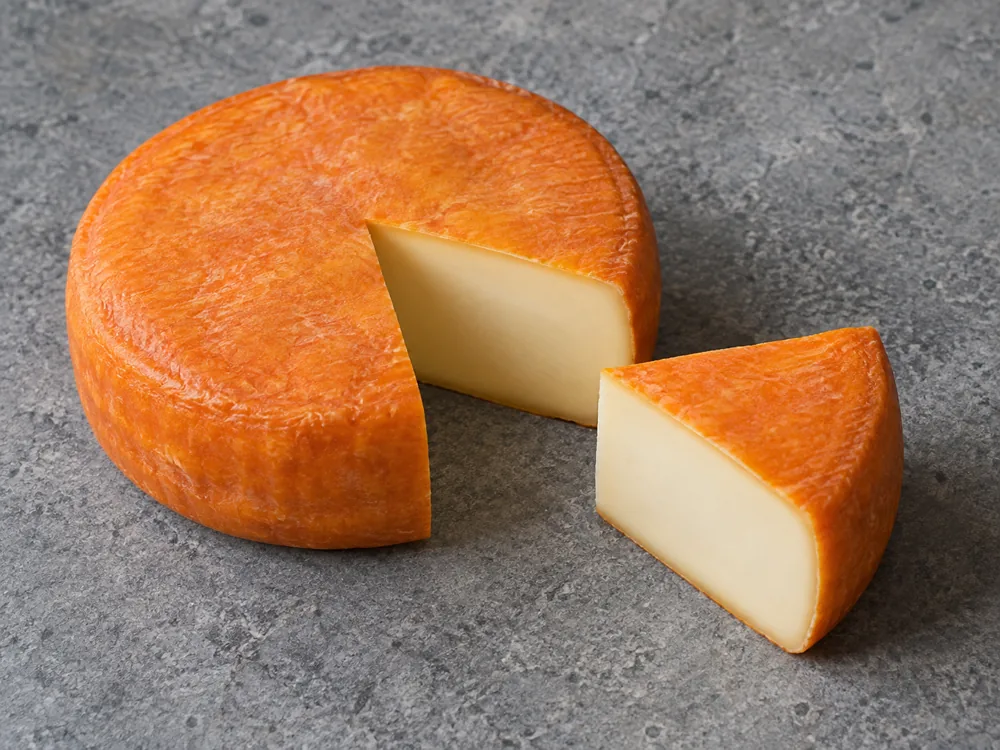Whole orange-rinded wheel with a one-sixth wedge cut out and set beside it - Keltic Gold | KnowTheCheese