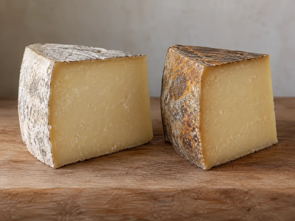 Two cut wedges side by side, one with a whitish to light grey rind and one with an amber brown rind - Laguiole | KnowTheCheese
