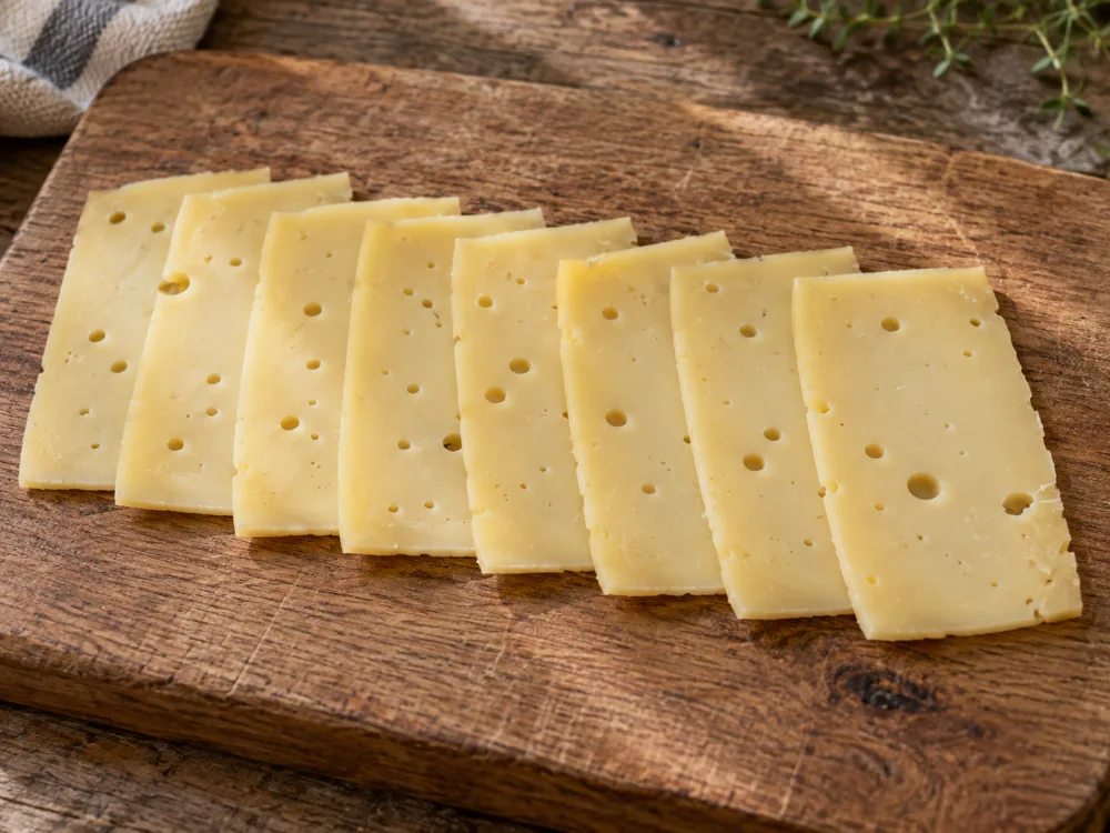 Eight thin slices of holed cheese in a row on a wooden board - Leerdammer | KnowTheCheese