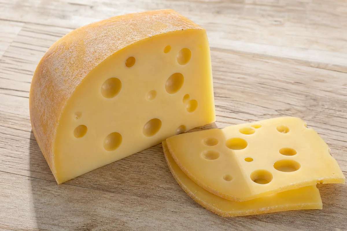 Wedge of Maasdam with smooth pale paste and large holes - Maasdam cheese | KnowTheCheese