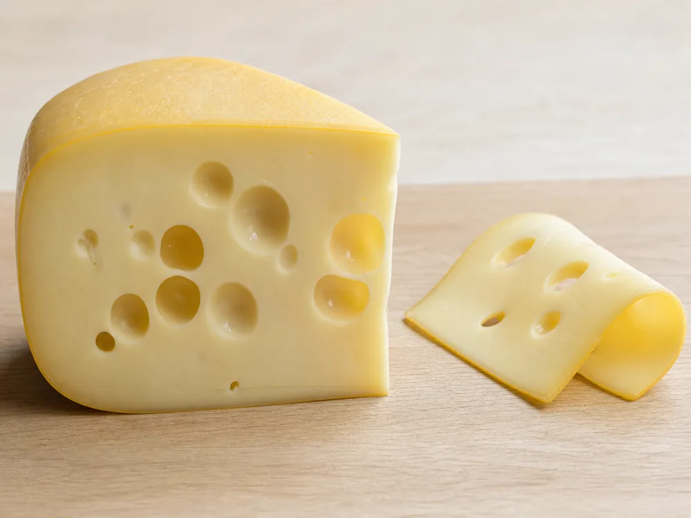 Maasdam wedge and bent slice showing large eyes and supple paste - Maasdam | KnowTheCheese