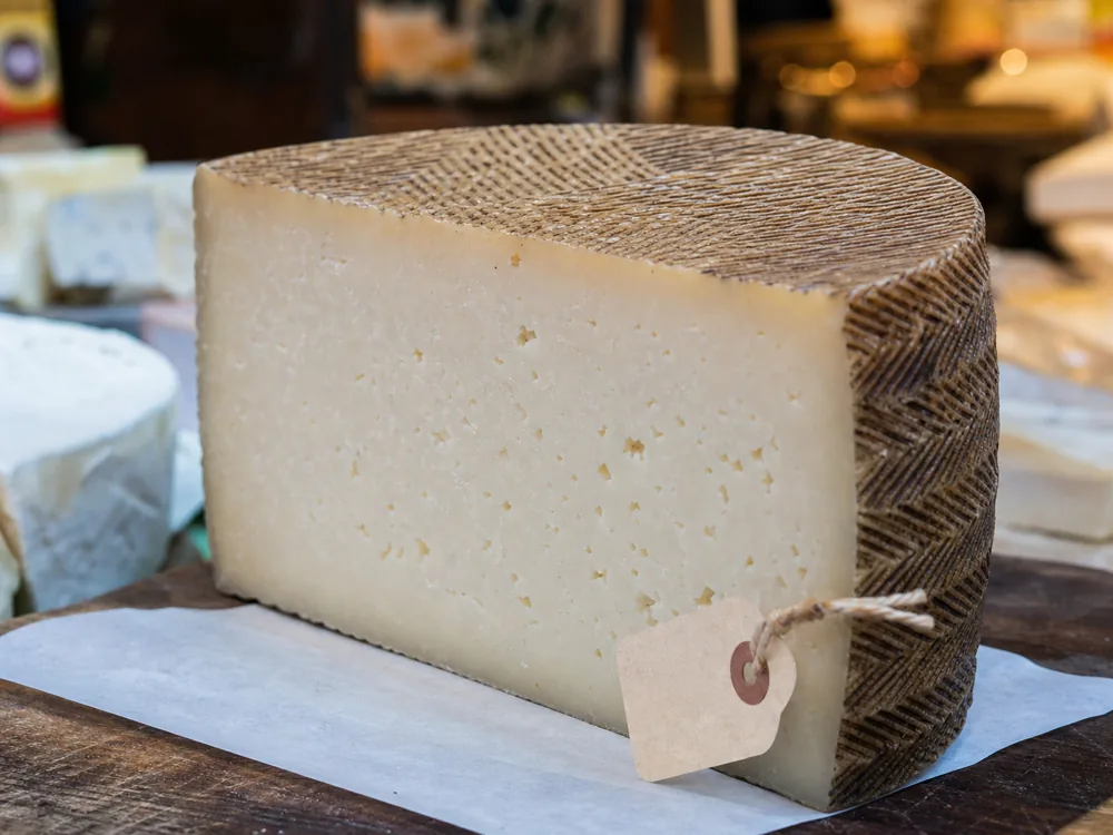 Manchego wedge showing crosshatch rind and compact sheep milk paste - Manchego cheese | KnowTheCheese