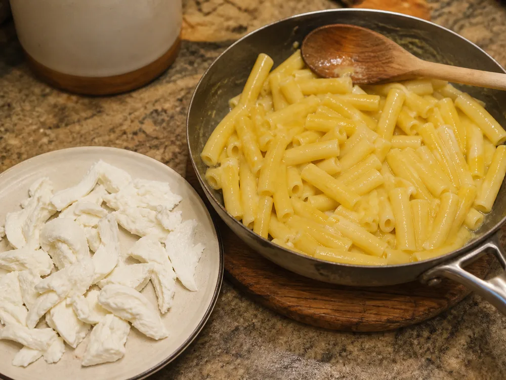Buttered pasta in a pan beside torn white stretched-curd cheese ready to melt in - Manteca | KnowTheCheese