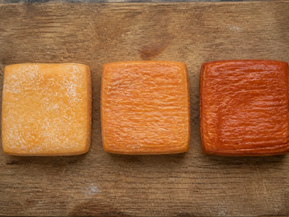 Three square washed-rind cheeses showing rind colour from pale yellow to deep red - Maroilles | KnowTheCheese