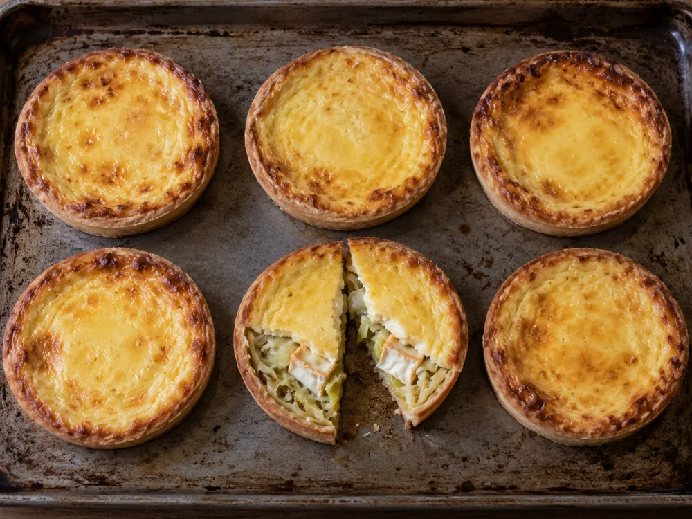Six small baked round tartlets with golden custard, one cut open to show leek and soft cheese pieces - Maroilles | KnowTheCheese