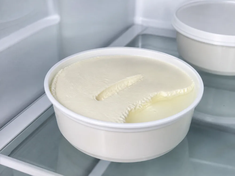 Opened mascarpone tub with a dense surface and a small clear whey puddle at one edge - Mascarpone | KnowTheCheese