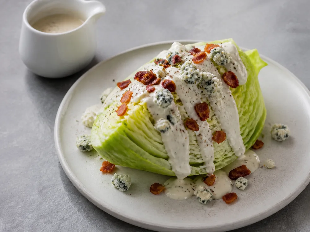 A wedge salad topped with blue cheese crumbles and thick dressing - Maytag Blue | KnowTheCheese