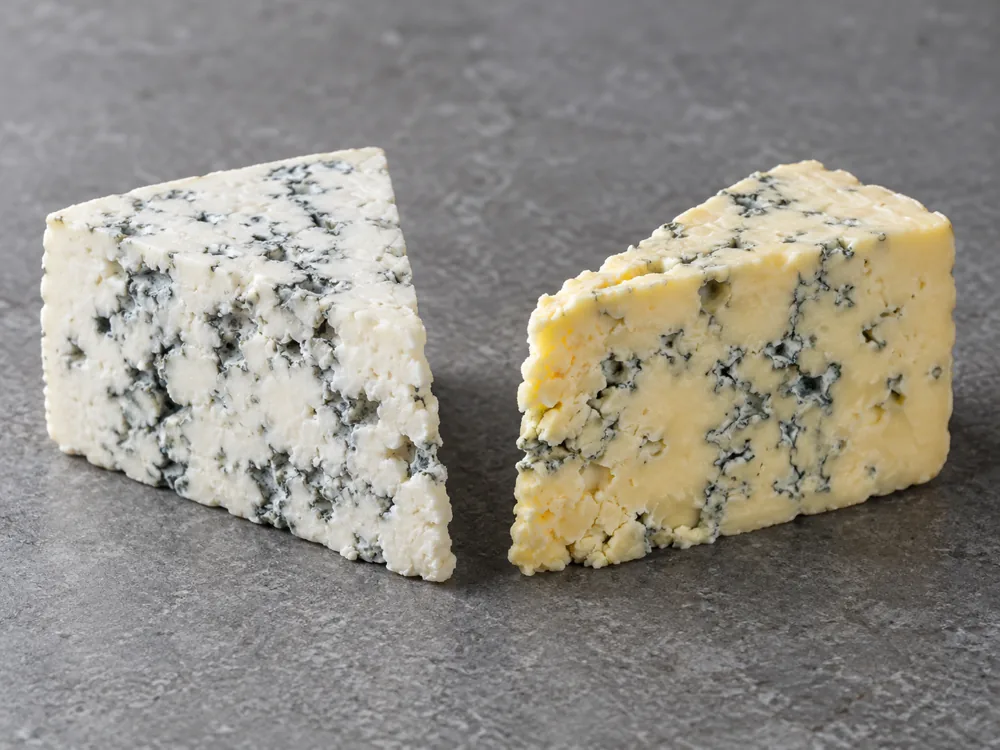 Two wedges of blue-veined cheese side by side, one with white paste and one with creamy yellow paste - Maytag Blue | KnowTheCheese