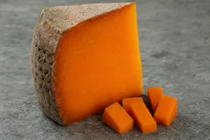 Wedge of aged Mimolette with bright-orange paste and pockmarked rind - Mimolette cheese | KnowTheCheese