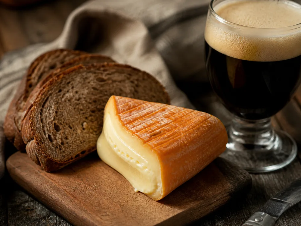 A wedge of orange-rinded soft cheese with dark bread and a glass of dark beer - Minger | KnowTheCheese