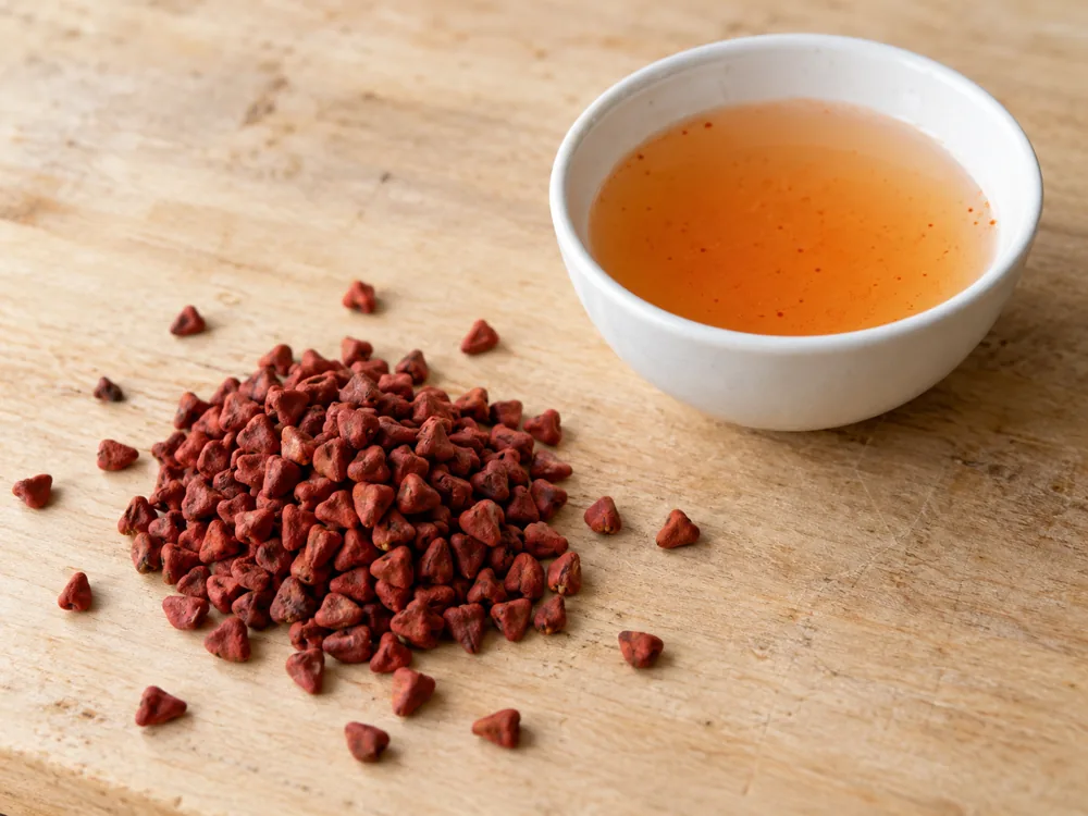 Heap of dry red annatto seeds beside a small bowl of orange liquid - Minger | KnowTheCheese