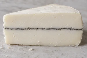 Cut face of a semi-soft bone-white cheese split by one thin dark ash line - Mobay | KnowTheCheese