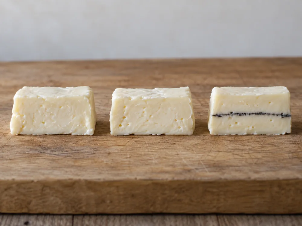 Three small pieces of bone-white cheese in a row, the first two plain and the third with one thin ash line through its middle - Mobay | KnowTheCheese
